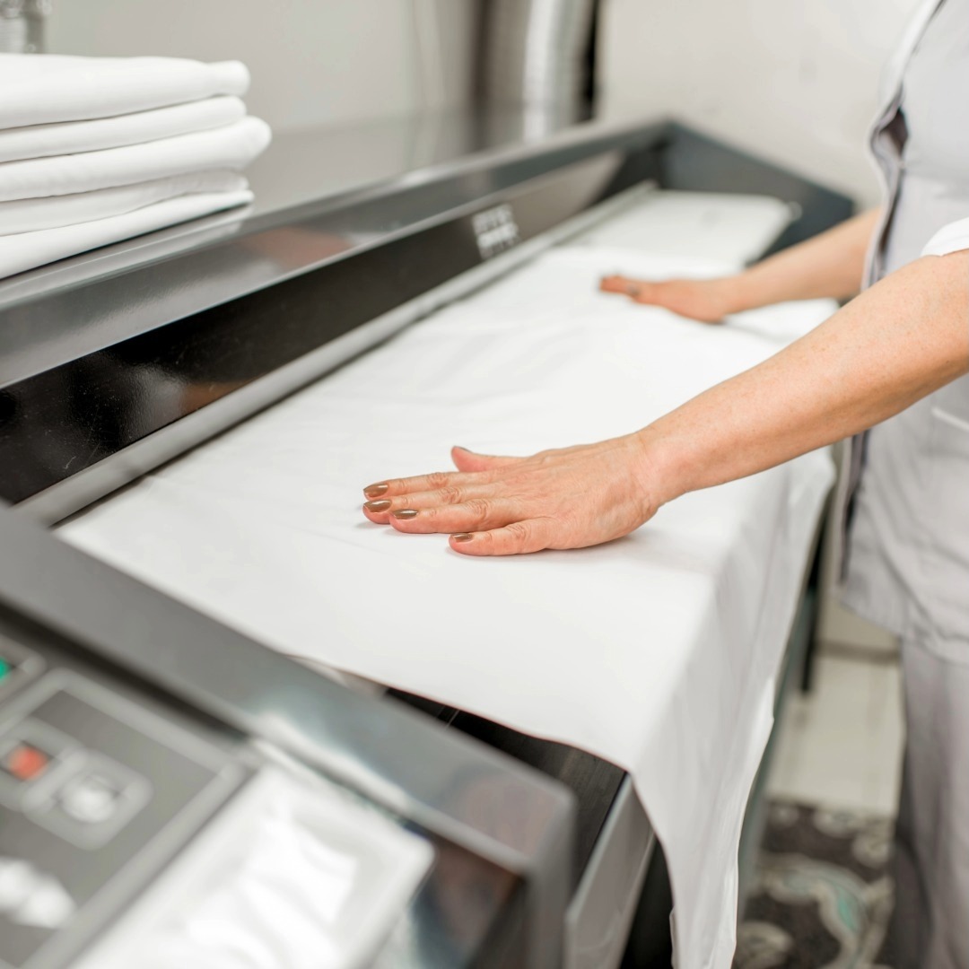 Mangano in funzione e mani di operatrice che stira un tessuto bianco.