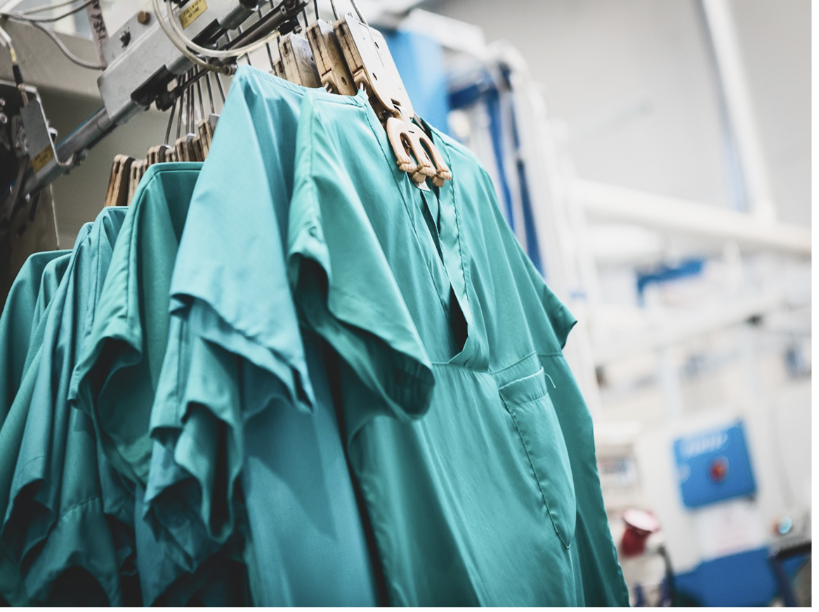 Divise ospedaliere appese su un macchinario di una lavanderia industriale.